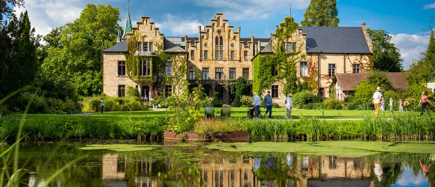 Schloss Ippenburg im Osnabrücker Land Historisches Gebäude mit Spitzgiebeln und bewachsenem Mauerwerk, Park und Teich im Vordergrund.