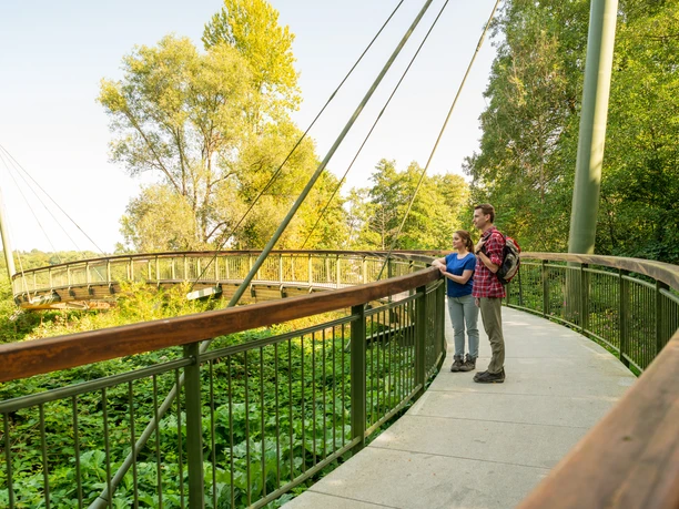Aggerbogen Ein Paar genießt den Ausblick auf einem grünen, baumbestandenen Baumwipfelpfad bei sonnigem Wetter.