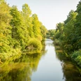 Aggerbogen Fluss fließt durch bewaldete Landschaft, Brücke im Hintergrund, sonniger Tag mit klarem Himmel.