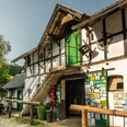 Gammersbacher Mühle Ein historisches Fachwerkgebäude mit grüner Tür, Holzdetails und umgeben von Bäumen bei Sonnenschein.