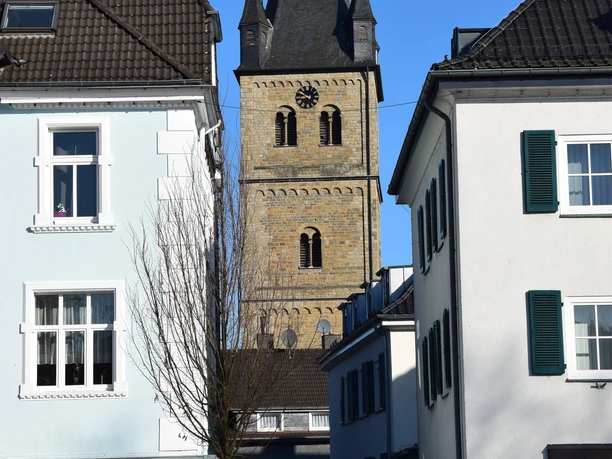Kirche St. Nikolaus <p>Historischer Kirchturm aus Bruchstein, eingerahmt von weißen Stadthäusern unter klarem, blauem Himmel.</p>