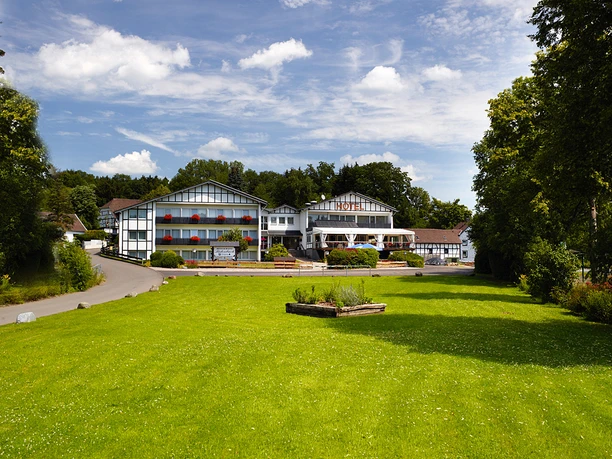 hotel-restaurant-luedenbach.jpg Ein traditionelles Hotel umgeben von üppigem Grün unter blauem Himmel und wenigen Wolken.