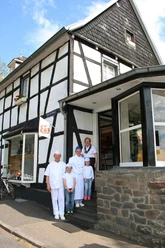 011 Kropppenberg Familie HN.JPG Vier Personen in weißer Arbeitskleidung stehen lächelnd vor einem traditionellen Fachwerkhaus.