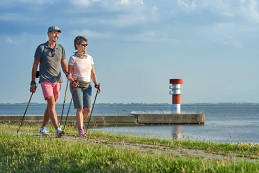 Entdeckerrunde maritimes Brunsbüttel Zwei Wandernde am Wasserweg vor kleinem Leuchtturm