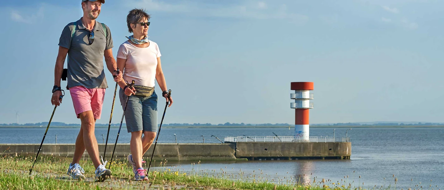 Entdeckerrunde maritimes Brunsbüttel Zwei Wandernde am Wasserweg vor kleinem Leuchtturm