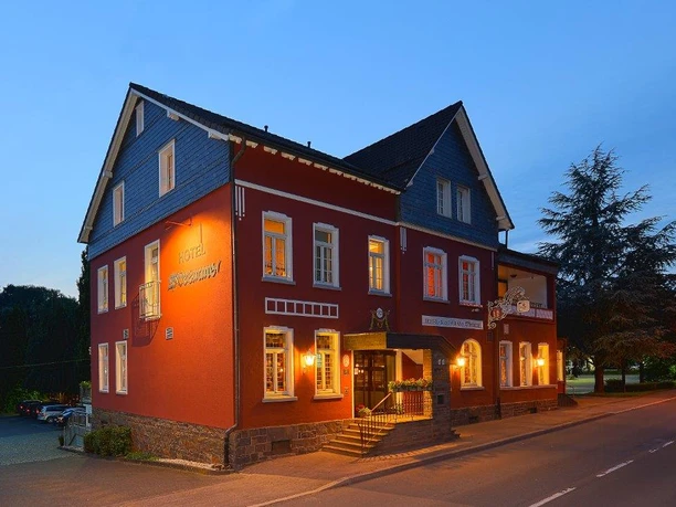 Außenansicht_Nacht Ein charmantes, beleuchtetes Hotel in einem klassischen Gebäude mit Schieferdach, bei Abenddämmerung.