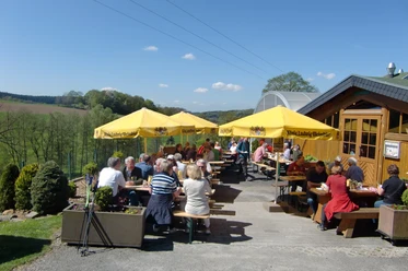 Biergarten-Tenne Menschen genießen bei sonnigem Wetter eine Mahlzeit auf einer Terrasse mit gelben Sonnenschirmen.
