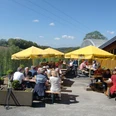 Biergarten-Tenne Menschen genießen bei sonnigem Wetter eine Mahlzeit auf einer Terrasse mit gelben Sonnenschirmen.