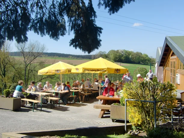 CIMG5628.JPG Menschen genießen ein sonniges Mittagessen unter gelben Sonnenschirmen auf einer Landterrasse.