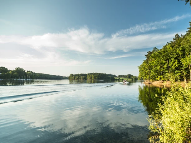 Bevertalsperre Ein ruhiger See an einem sonnigen Tag, umgeben von bewaldeten Ufern und einem strahlend blauen Himmel.