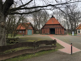 Ein traditionelles Fachwerkhaus mit roten Ziegeln, umgeben von Bäumen und mit einem gepflasterten Weg.
