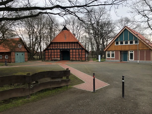 Traditionelles Fachwerkhaus mit rotem Backstein und spitzem Dach, umgeben von Bäumen und Natur.