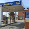 Tankstelle Poppinga Greetsiel Kleine freie Tankstelle mit Zapfsäulen, gelb-blauem Dach und Backsteinhaus im Hintergrund.