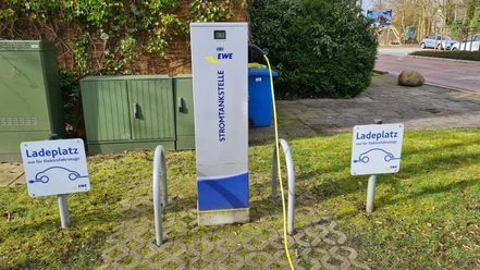 Öffentlicher Parkplatz Rathaus Pewsum Öffentliche EWE-Stromtankstelle mit Ladekabel und Schildern für Elektrofahrzeuge.