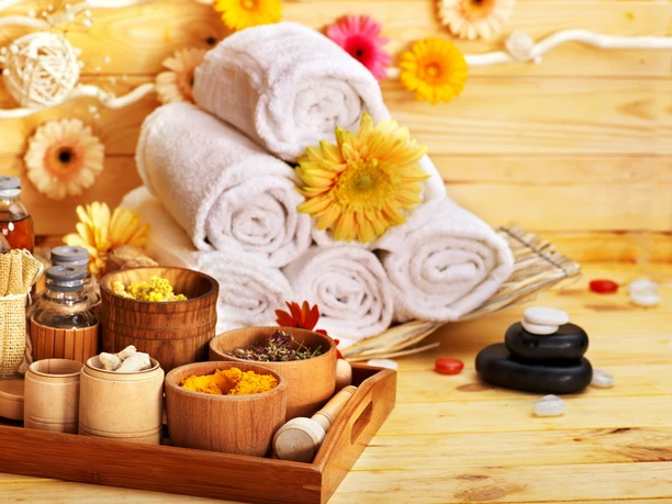 Wellness und Entspannung Mehrere weiße Handtücher in einem Korb, frische Blumen und Wellness-Accessoires auf Holzuntergrund.