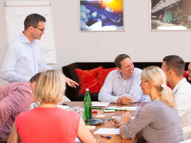 Holger-Krebs-Workshops-Foto-Enric-Mammen-36-von-95.jpg Eine Gruppe von Menschen in einem Konferenzraum, die an einem Workshop teilnehmen und lächeln.