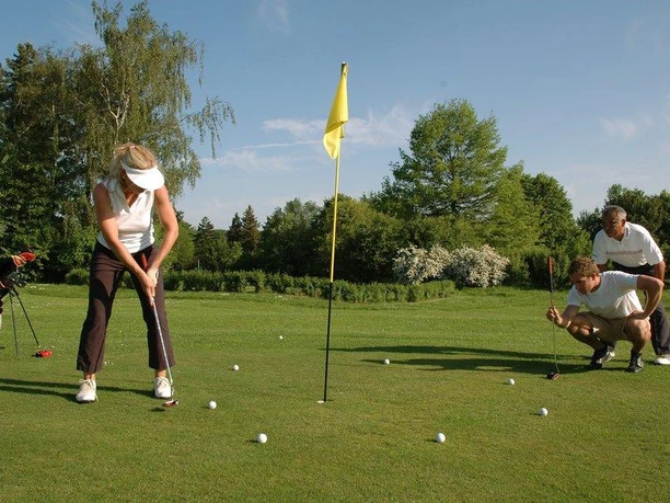 index_01.jpg Personen beim Golfen auf grünem Rasen mit Bäumen im Hintergrund an sonnigem Tag.