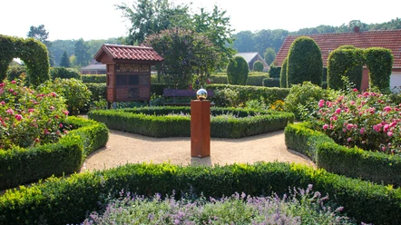 Bauerngarten Lorup Symmetrischer Bauerngarten mit Rosen, Buchshecken, Blumenbeeten und Insektenhotel im Sommerlicht.