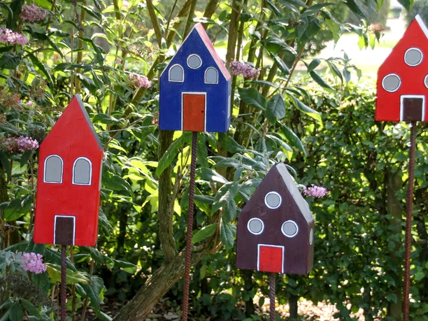 Bauerngarten Lorup Bunte Holzhausfiguren auf Stäben zwischen blühenden Pflanzen in einem grünen Bauerngarten.