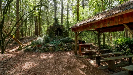 Fleers Grotte Stein-Grotte mit Marienstatue im Wald, daneben überdachter Andachtsplatz mit Holzbänken.