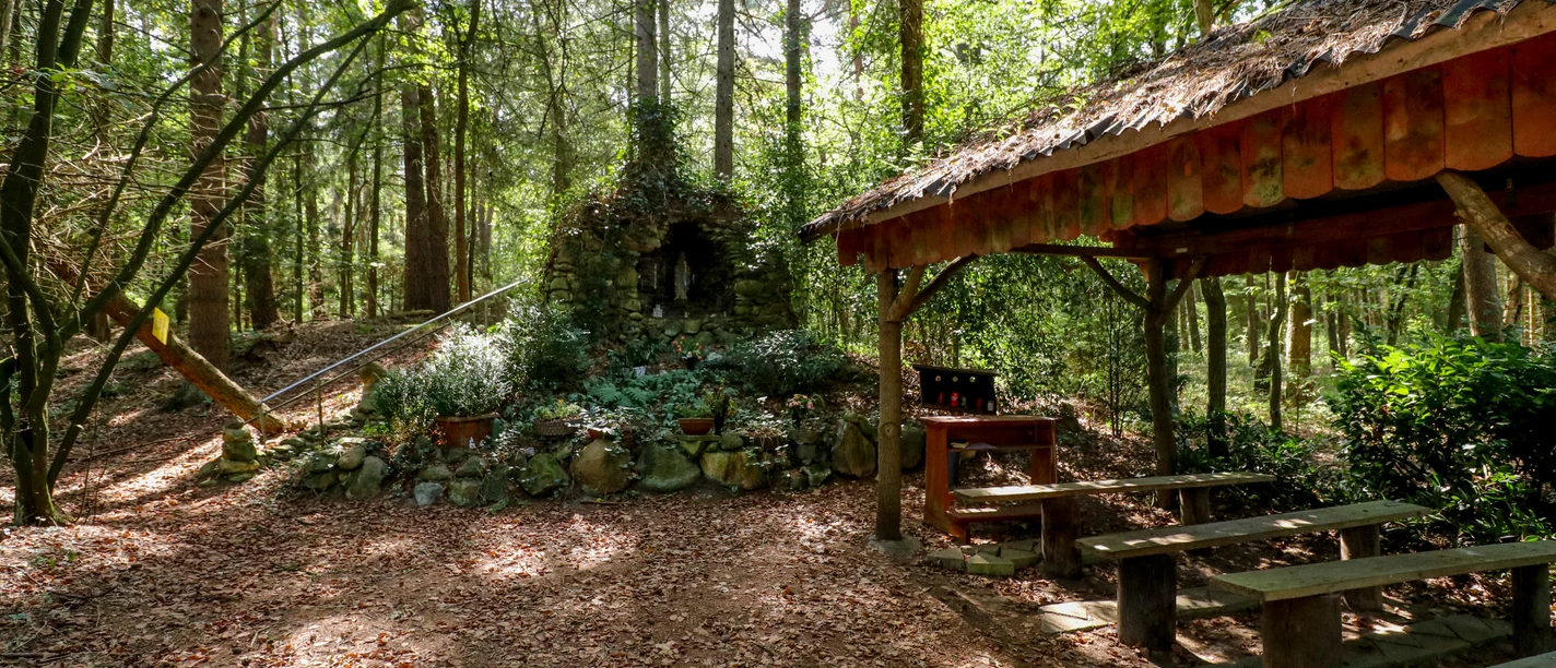Fleers Grotte Stein-Grotte mit Marienstatue im Wald, daneben überdachter Andachtsplatz mit Holzbänken.
