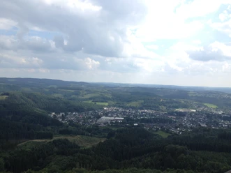 Streifzug Feuer- und Flammeweg <p>Luftaufnahme von Bergneustadt, umgeben von grünen Wäldern und sanften Hügeln unter wolkigem Himmel.</p>