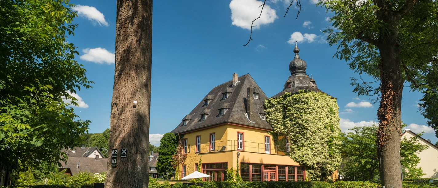 Burg Zweiffel Historisches gelbes Gebäude mit runder Kuppel und Garten in Bergisch Gladbach bei sonnigem Himmel.