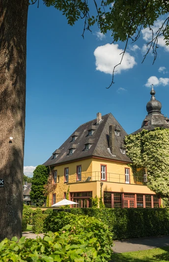 Burg Zweiffel Historisches gelbes Gebäude mit runder Kuppel und Garten in Bergisch Gladbach bei sonnigem Himmel.
