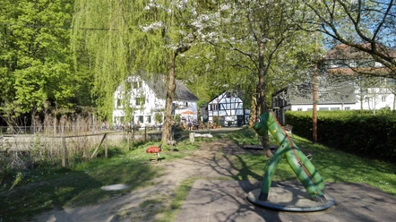 Alte Dombach Ein grüner Spielplatz mit Schaukelpferd, umgeben von Bäumen und traditionellen Fachwerkhäusern.