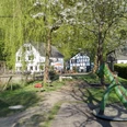Alte Dombach Ein grüner Spielplatz mit Schaukelpferd, umgeben von Bäumen und traditionellen Fachwerkhäusern.