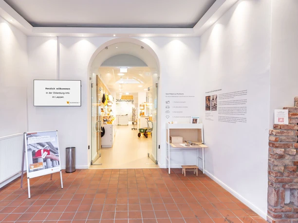 Vom Eingangsbereich der Oldenburg-Info, der Innenraum dess Turmes, ist der Blick in Richtung Touristinfo gegeben. Rechts im Vordergrund ist die Hoerstation zu sehen, links ein Plakataufsteller.
