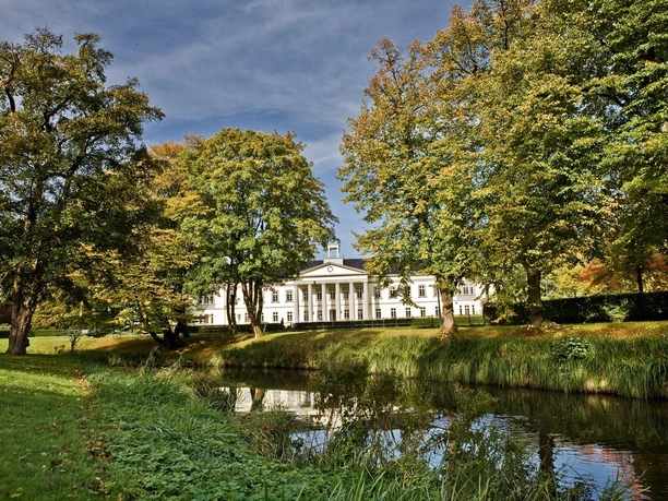 PFL Oldenburg im Hintegrund umgeben von einer grünen Wiese und grünen Bäumen