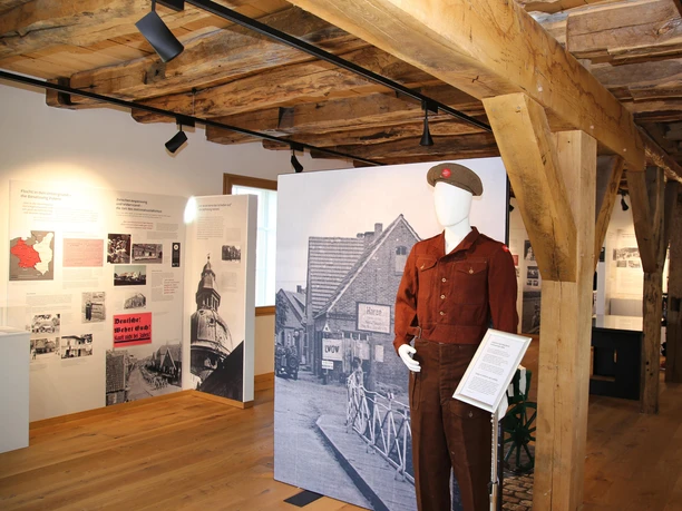 Museum Inselmühle Ausstellungsraum mit Holzdecke, historischen Informationstafeln und Uniformfigur zur Nachkriegszeit