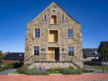 Museum Inselmühle Steinerne Fassade der Inselmühle Haren mit Treppenaufgang, bunten Blumenbeeten und blauem Himmel.