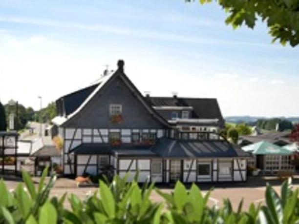 Hotel Napoleon Fachwerkhaus mit steilem Schieferdach, umgeben von grünen Bäumen und blauem Himmel in ländlicher Umgebung.