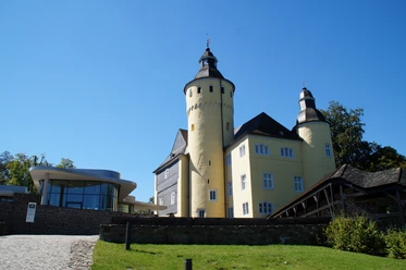 Schloss Homburg Burg Nümbrecht im Sonnenschein, links moderner Anbau, umgeben von grüner Landschaft.