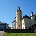 Schloss Homburg Burg Nümbrecht im Sonnenschein, links moderner Anbau, umgeben von grüner Landschaft.