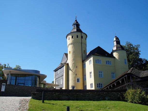 Schloss Homburg Burg Nümbrecht im Sonnenschein, links moderner Anbau, umgeben von grüner Landschaft.