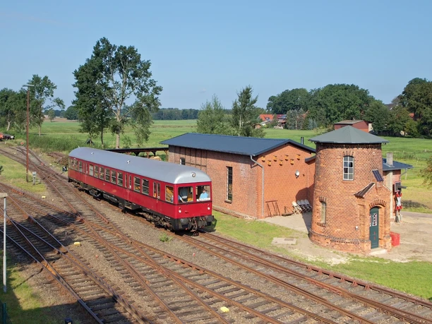 Heide-Express Roter historischer Triebwagen des Heide-Express passiert alte Backsteingebäude und Gleisanlagen.