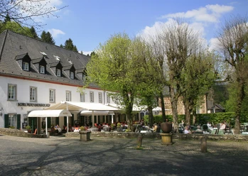 Altenberger Hof Ein charmantes Hotel mit Terrasse, umgeben von Bäumen, Gäste genießen die Sonne bei Getränken.