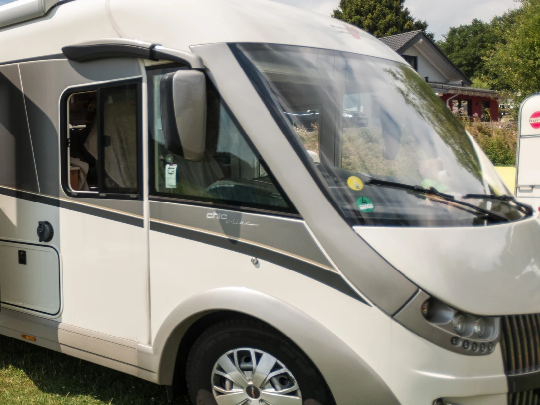 Campingpark im Bergischen Land Wohnmobil auf einem grünen Stellplatz mit Bäumen im Hintergrund in einer ländlichen Umgebung.