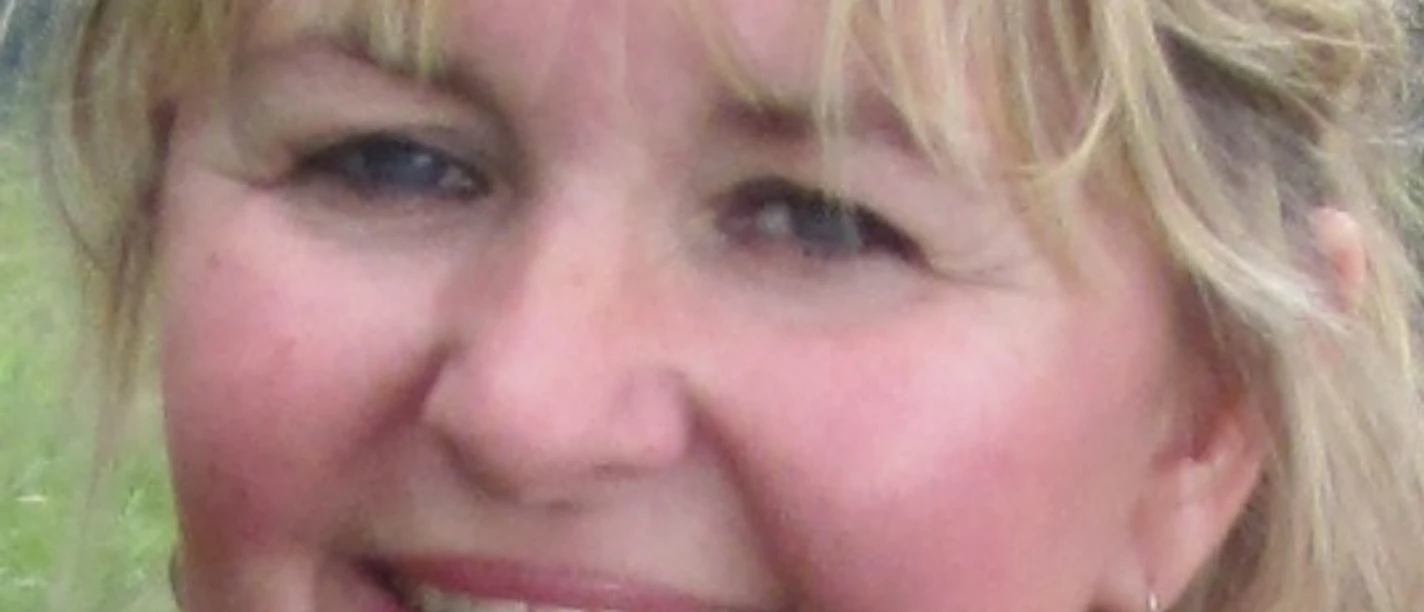 Sylvia Bensch.jpg Lächelnde Frau mit blonden Haaren und Sonnenbrille im Haar in einer bergigen Landschaft.
