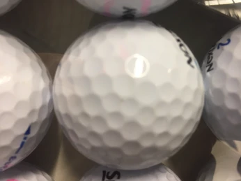 Golfbälle Nahaufnahme eines weißen Golfballs mit strukturierter Oberfläche und schwarzem Aufdruck, von sanftem Licht beleuchtet.