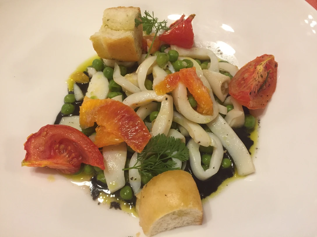 Meeresfrüchte Ein Teller mit Tintenfischringen, Erbsen, Orangenscheiben und gerösteten Tomaten, garniert mit Brot.