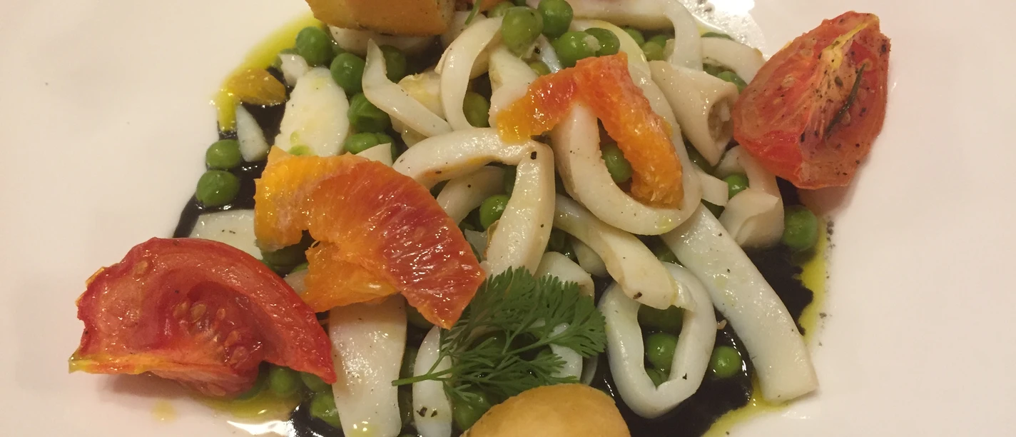 Meeresfrüchte Ein Teller mit Tintenfischringen, Erbsen, Orangenscheiben und gerösteten Tomaten, garniert mit Brot.