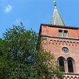 Nikolaikirche Pewsum Roter Backsteinturm der Nikolaikirche Pewsum mit Uhr und Spitzdach vor blauem Himmel.