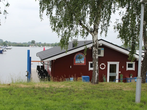 Wieltsee Smokey Island Ein gemütliches rotes Gebäude am Ufer, umgeben von Bäumen, empfängt Besucher am Wieltsee.