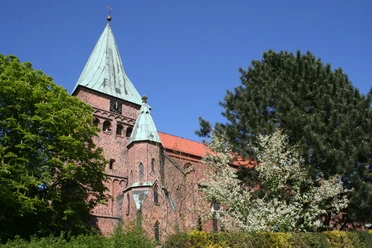 A red brick church with a green copper tower, surrounded by trees under a blue sky in Weyhe.
