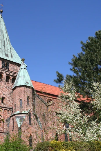 Eine rote Backsteinkirche mit grünem Kupferturm, umgeben von Bäumen unter blauem Himmel in Weyhe.