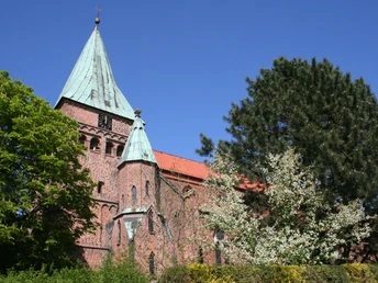 FelicianusKirche Weyhe Eine rote Backsteinkirche mit grünem Kupferturm, umgeben von Bäumen unter blauem Himmel in Weyhe.
